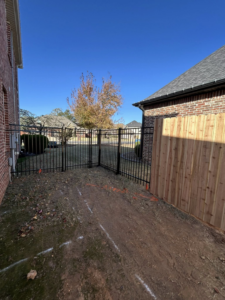 A newly installed black metal fence and wooden privacy fence in a residential backyard by Timber Wolf Fence Co. in Rogers, AR.