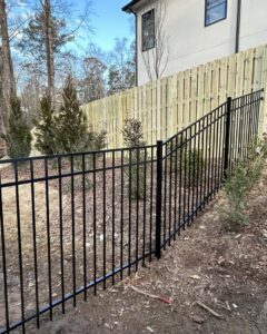 Black ornamental metal fence in the foreground with a tall wooden privacy fence in the background by Georgia Select Fence in Senoia, GA.