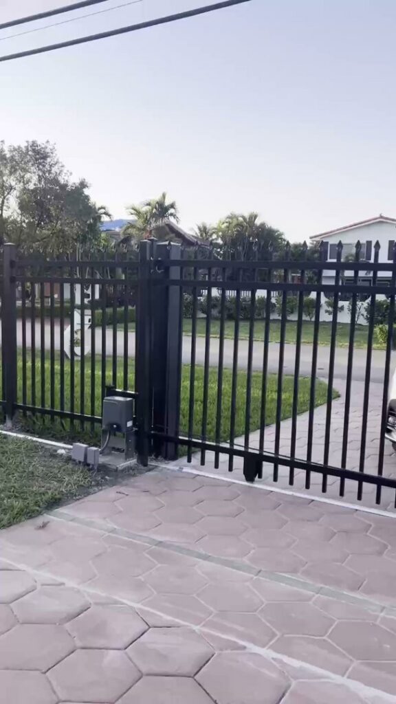 An automatic black metal sliding gate with an opener for property access by ARE FENCE LLC in Miami, FL.