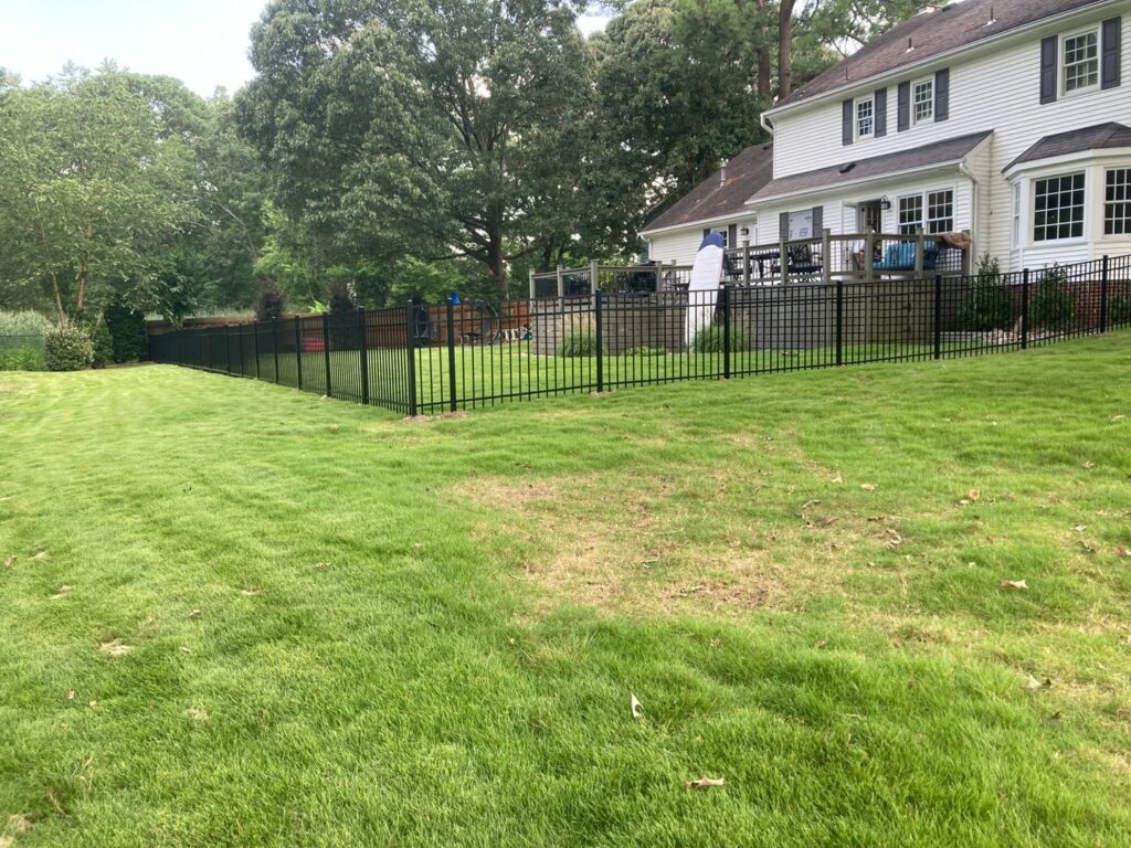 A black metal fence enclosing a large backyard with a deck installed by Sea Level Fence in Harbinger, NC