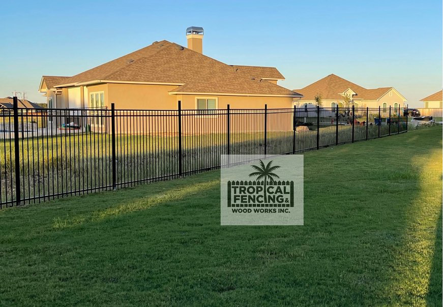 A long black metal fence installed around a residential backyard by Tropical Fencing And Wood Works in Page, TX.