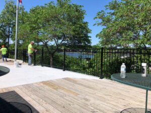 Workers installing a black metal railing along a deck overlooking water by Van's Fence in Kansas City, MO.