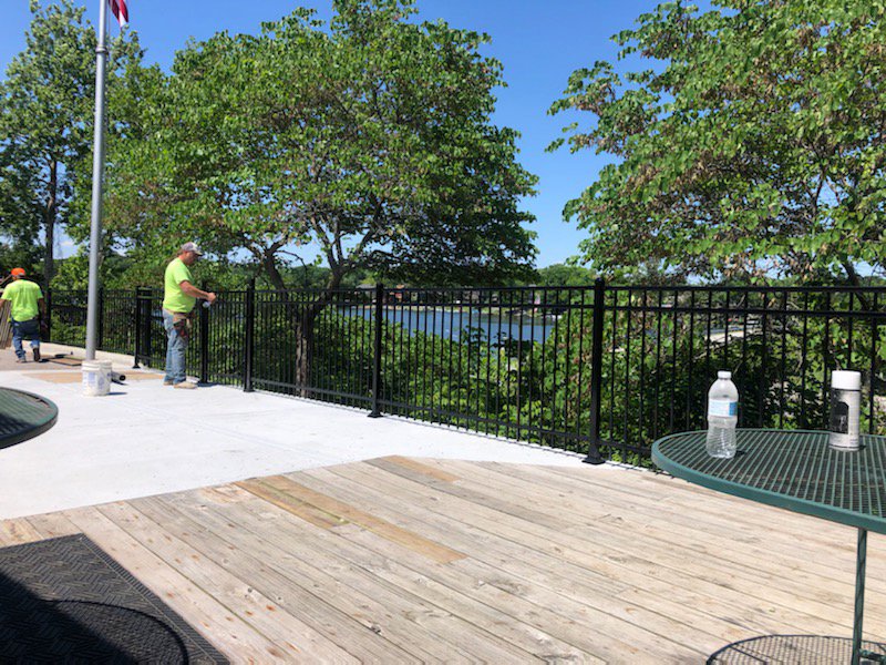 Workers installing a black metal railing along a deck overlooking water by Van's Fence in Kansas City, MO.