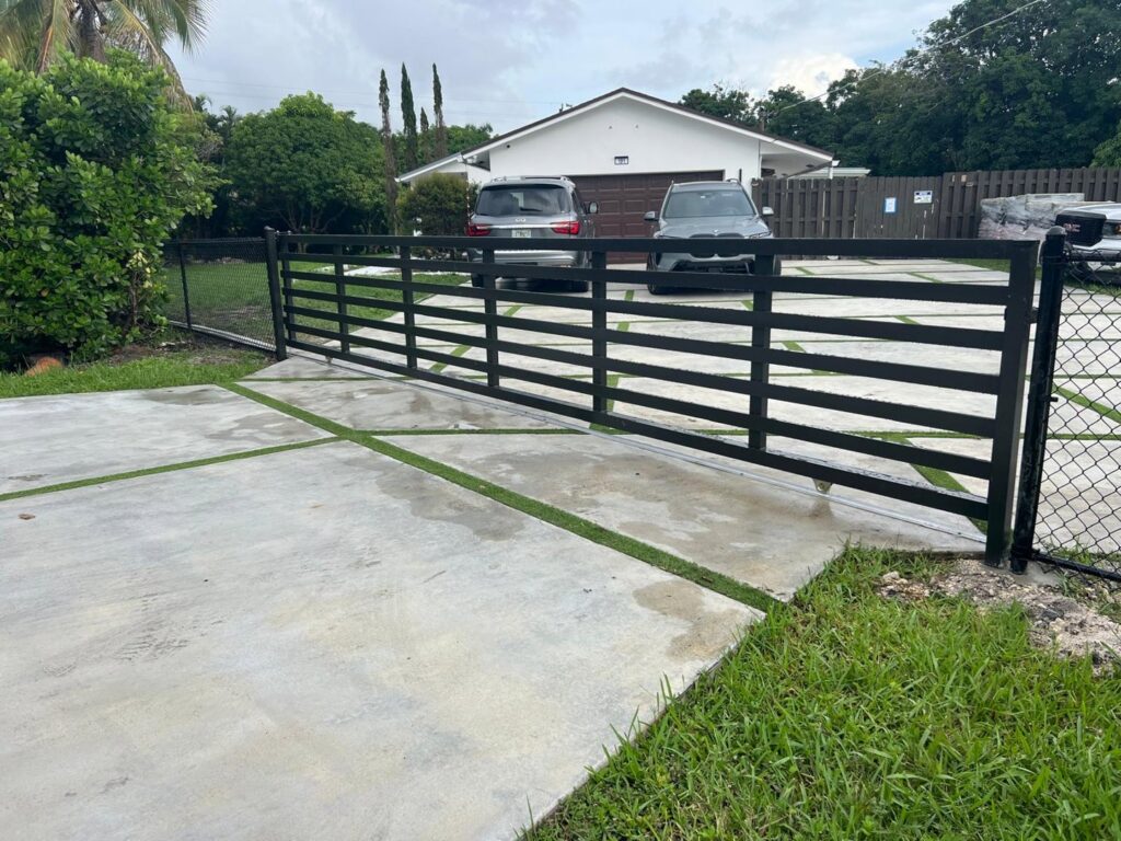 A black metal driveway gate with chain link fencing installed by Palm's Fence of Miami, FL.