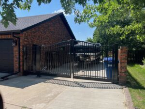 A black metal driveway gate installed next to a brick garage by Western Fence in Hebron, ND.