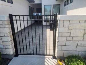 A black metal entry gate with a keypad installed into a stone wall by Josey's Fencing LLC in Caldwell, ID.