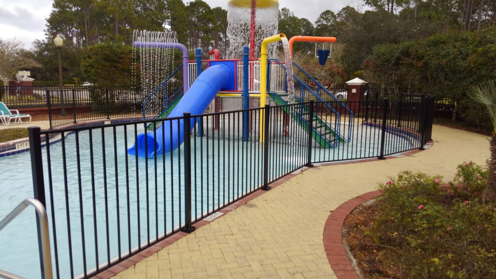 A black metal fence installed around a community pool and splash pad by Best Fence and Rail in Jacksonville, FL.