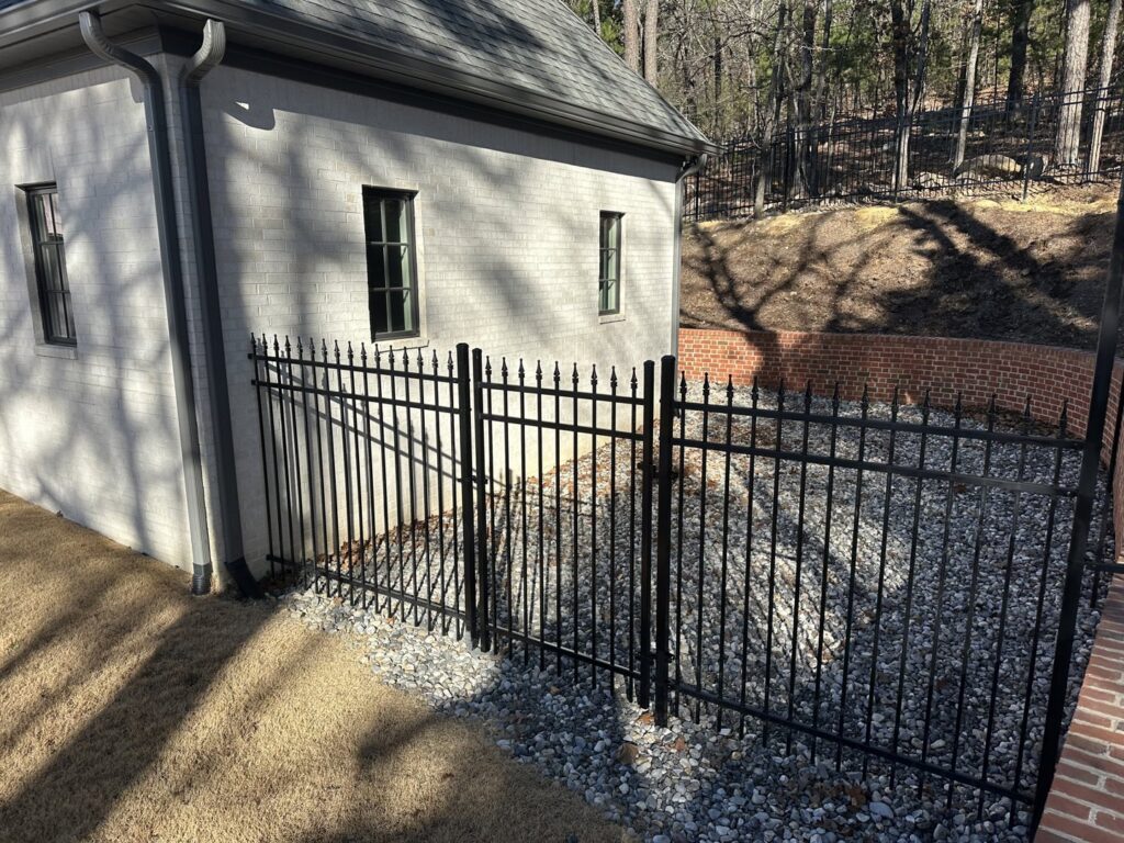 A black metal fence installed around a house, adjacent to a brick retaining wall, by Superior Fence and Rail of Little Rock, AR