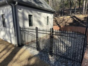 A black metal fence installed around a house, adjacent to a brick retaining wall, by Superior Fence and Rail of Little Rock, AR