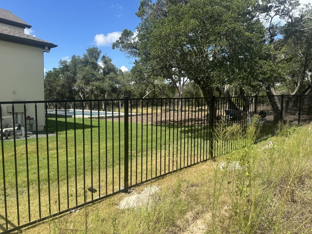 A black metal fence installed in a large grassy backyard with a swimming pool in the distance by Landmark Fence & Deck Company in Saint Paul, MN.