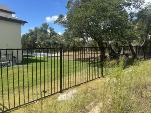 A black metal fence installed in a large grassy backyard with a swimming pool in the distance by Landmark Fence & Deck Company in Saint Paul, MN.