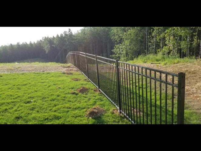 A sleek black metal fence installed in a large open field by Integrity Construction and Fencing, LLC in Clanton, AL.