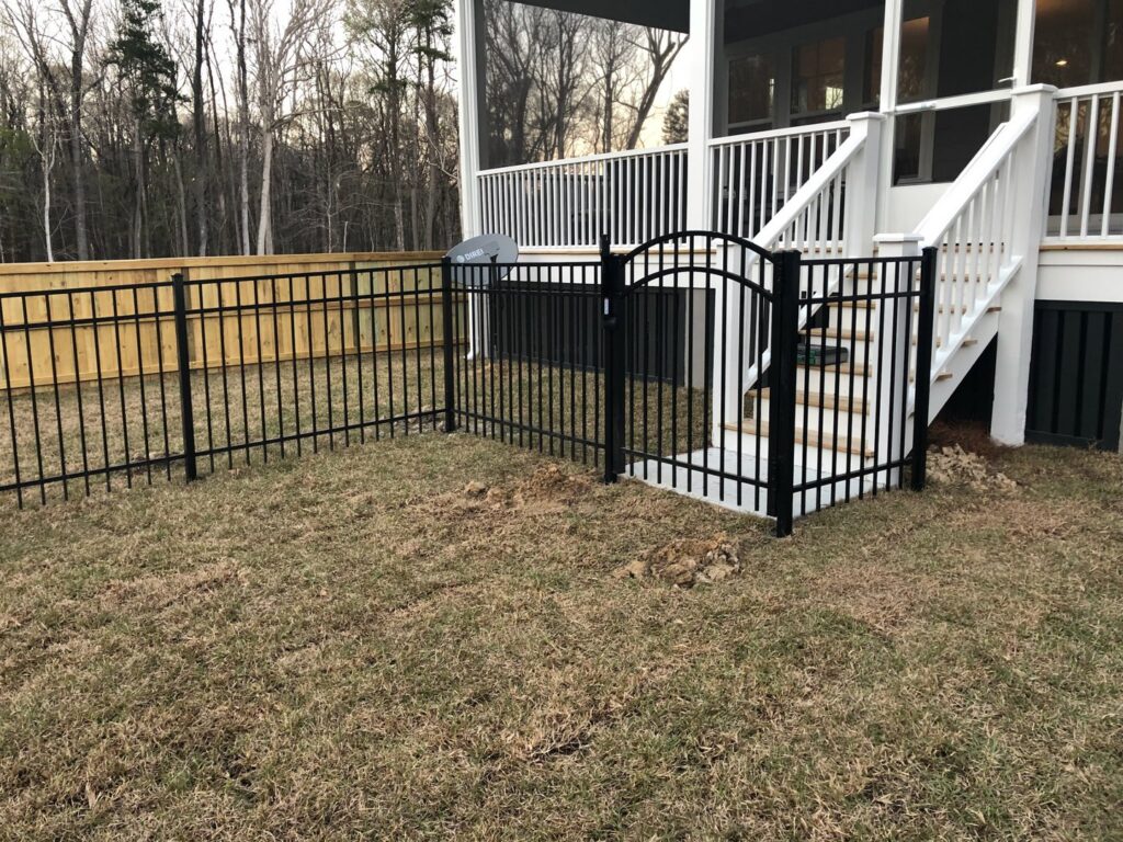 A black metal fence with a gate installed near a deck staircase, alongside a wood privacy fence by Charleston Fencing Services in Moncks Corner, SC.