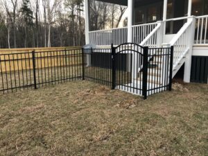A black metal fence with a gate installed near a deck staircase, alongside a wood privacy fence by Charleston Fencing Services in Moncks Corner, SC.
