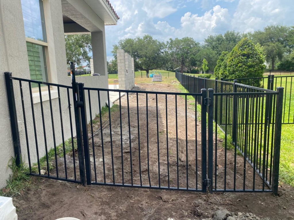A black metal fence with a gate being installed next to a residential property by Native Outdoors, LLC in Orlando, FL.