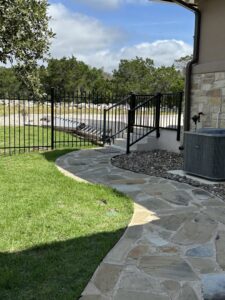 A black metal fence with a gate and stairs leading to a house by Liberty Fence & Stain in San Antonio, TX.