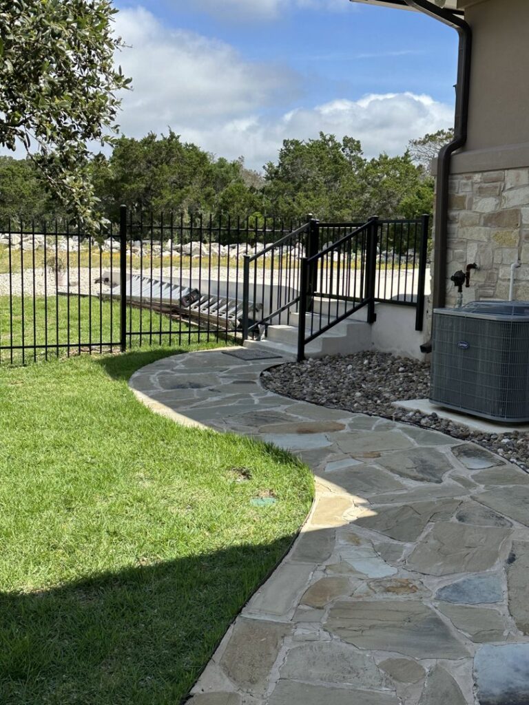 A black metal fence with a gate and stairs leading to a house by Liberty Fence & Stain in San Antonio, TX.