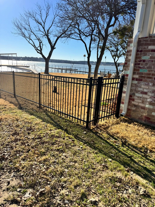 A black metal fence with a matching gate installed near a lake by B & S Fence Company in Haltom City, TX