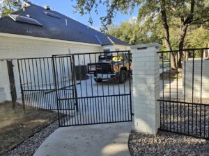 Black metal fence and gate installed alongside a white brick house, showcasing work by QD & E Fencing in Fort Worth, TX.