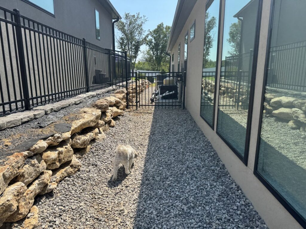 A black metal fence installed along a gravel path next to a modern residential home by Frontline Fence Company in Fulton, NY