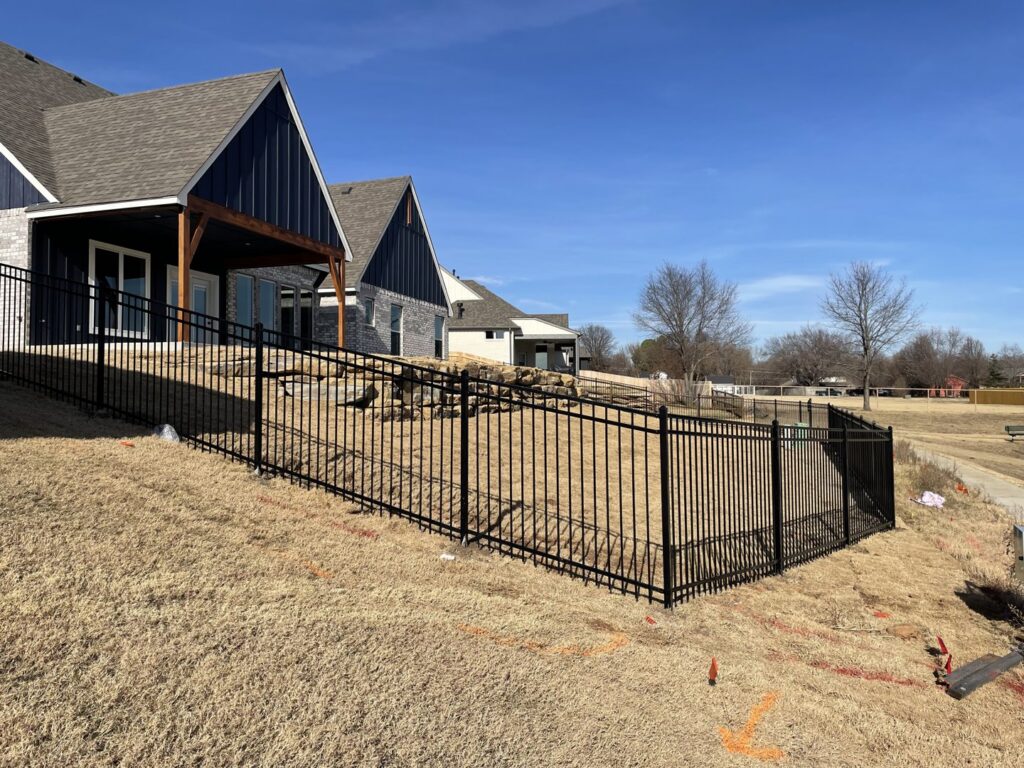 A black metal fence installed on a sloped residential property by Frontline Fence Company in Fulton, NY