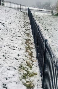 A newly installed black metal fence running down a snowy hill by B&L Fence Co in Youngstown, OH.