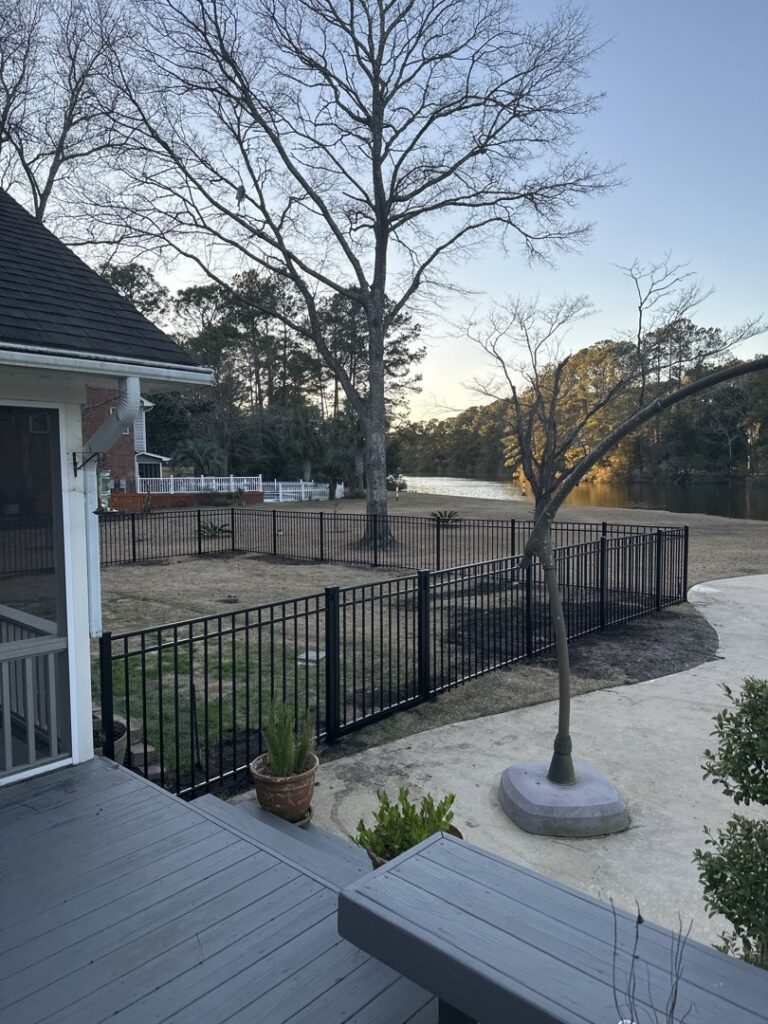 A black metal fence installed along the edge of a lake or pond, viewed from a residential deck by Five Star Fence in Charleston, SC.