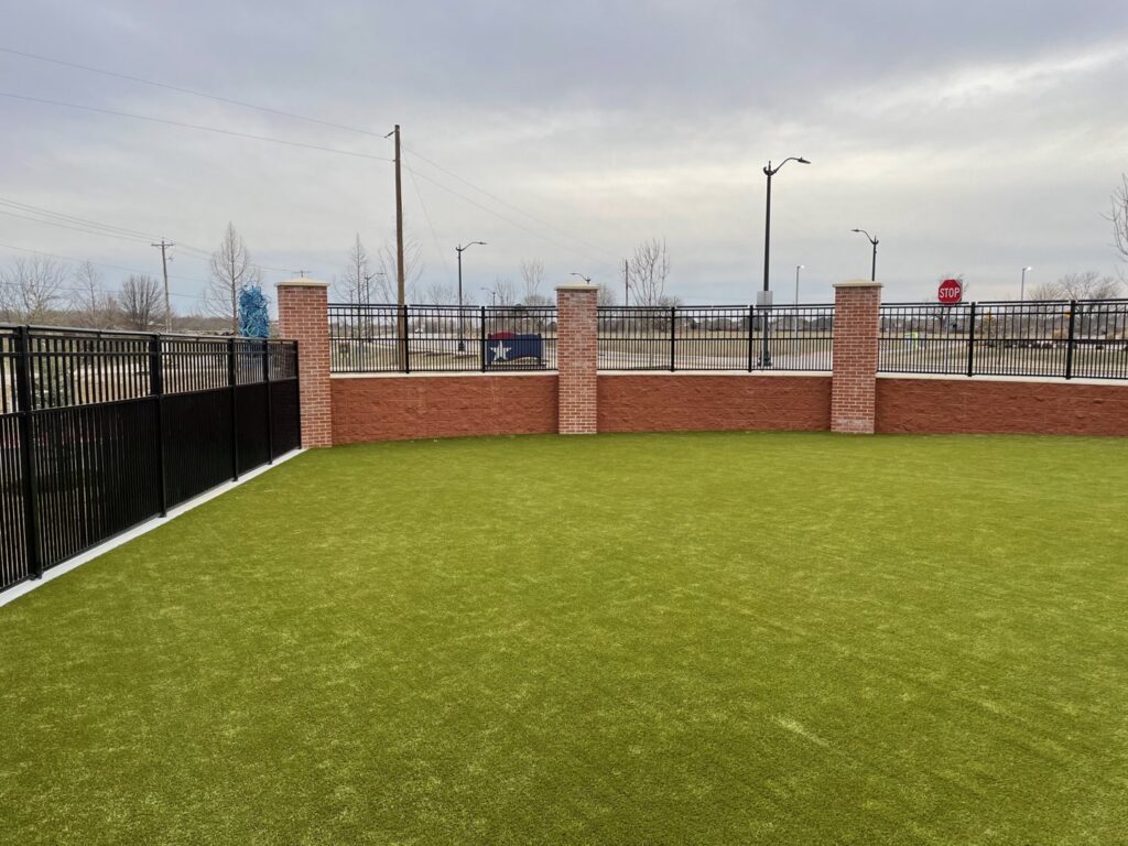 A black metal fence installed on a decorative brick wall around an artificial turf area by The Fence Man in Fort Smith, AR