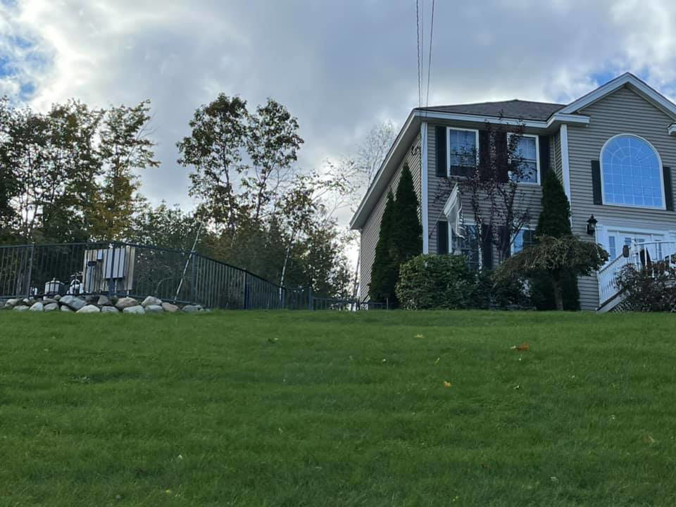 A black metal fence installed on a sloped residential yard near a house, completed by David Platania Fence in Derry, NH.