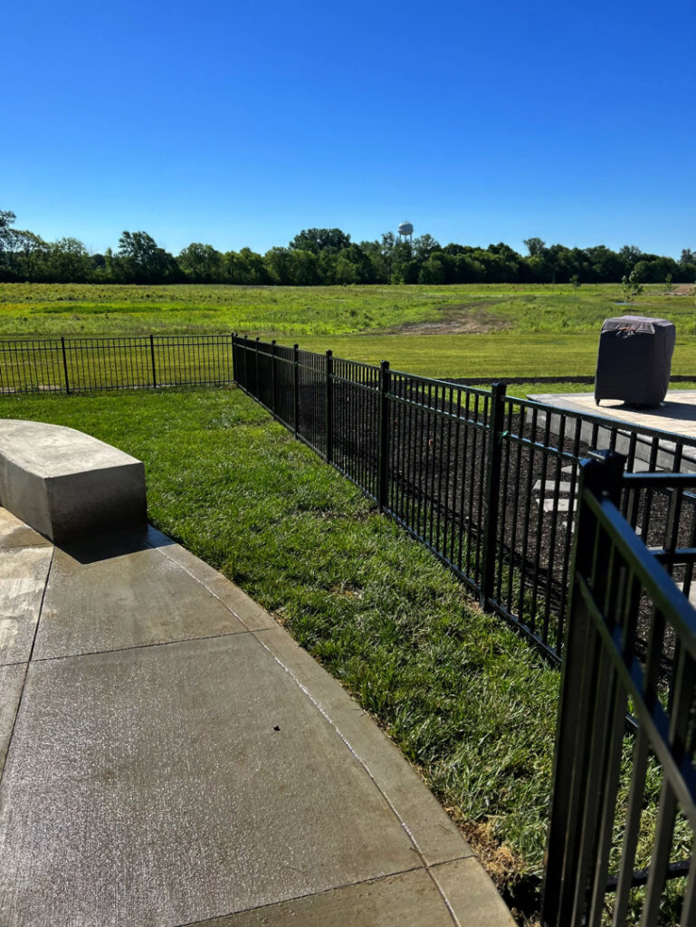 A black metal fence installed alongside a concrete patio, offering views of a field, by ReliableFencing in Columbus, OH.