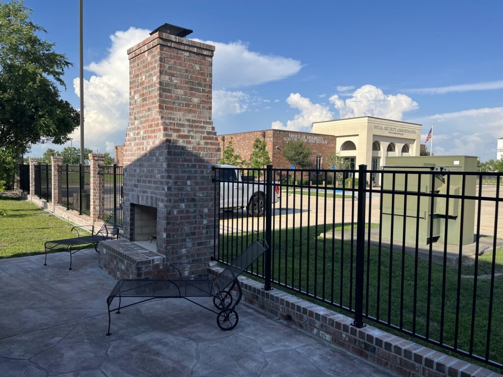 A black metal fence enclosing an outdoor patio area with a brick fireplace, installed by Southern Fencing, LLC in Houma, LA.