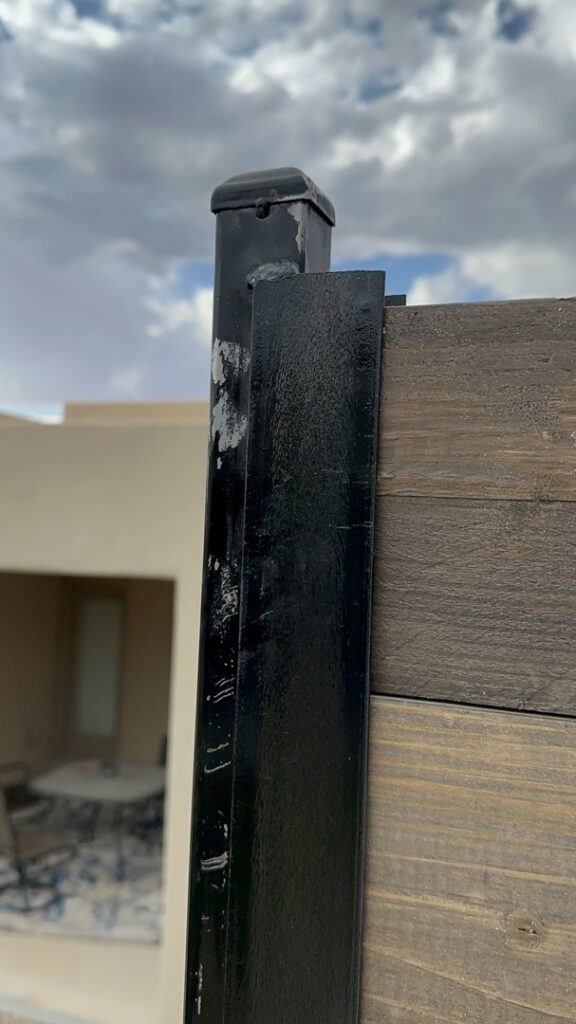 A close-up view of a black metal fence post with a top cap and horizontal wood planks installed by MJ Custom Fencing in Las Cruces, NM.