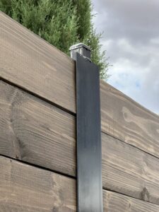 A close-up view of a black metal fence post supporting horizontal wood planks installed by MJ Custom Fencing in Las Cruces, NM.
