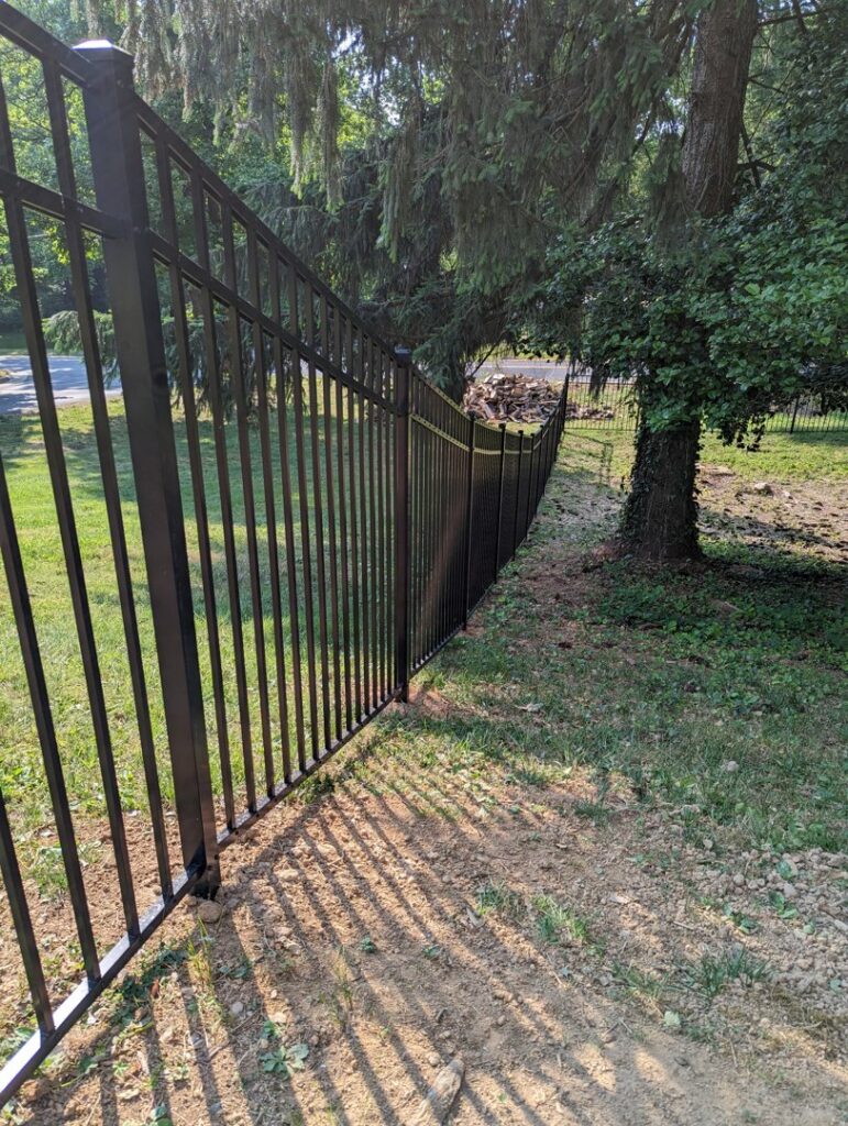 A newly installed black metal fence along a property line under trees by Concord Fence Llc in Wilmington, DE