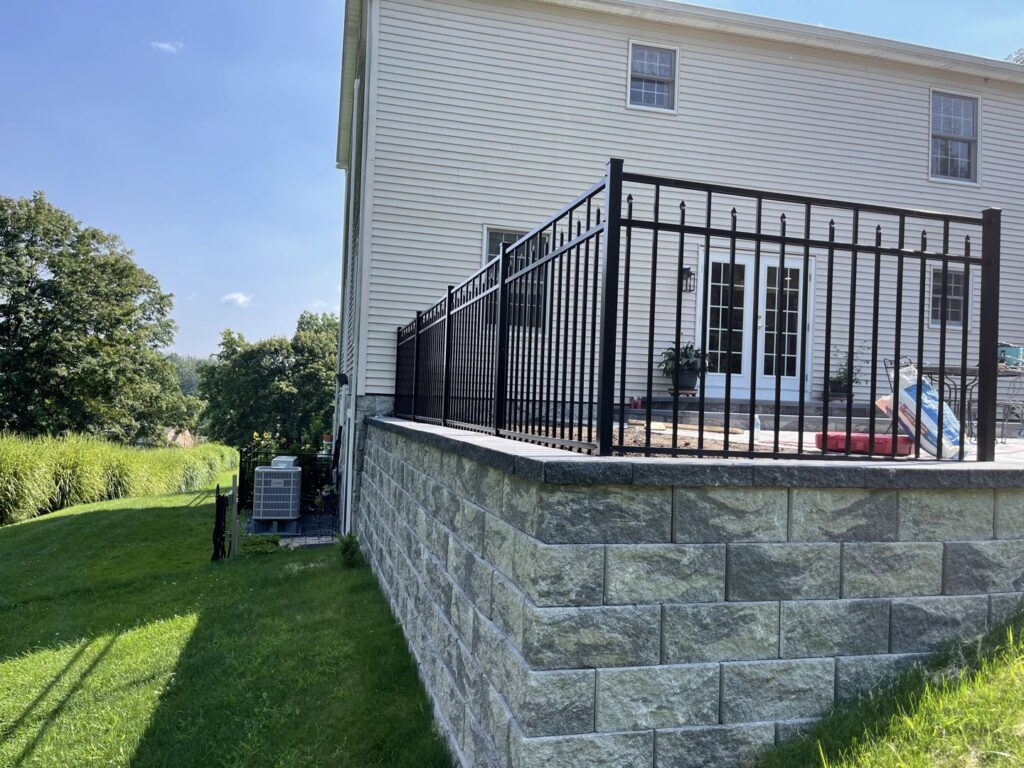 A durable black metal fence installed on top of a stone retaining wall by RP Fencing & Gates in Brewster, NY