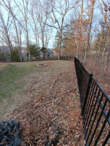 A black metal fence installed along a sloped backyard with a fire pit in the distance by Fence Experts STL in Fenton, MO