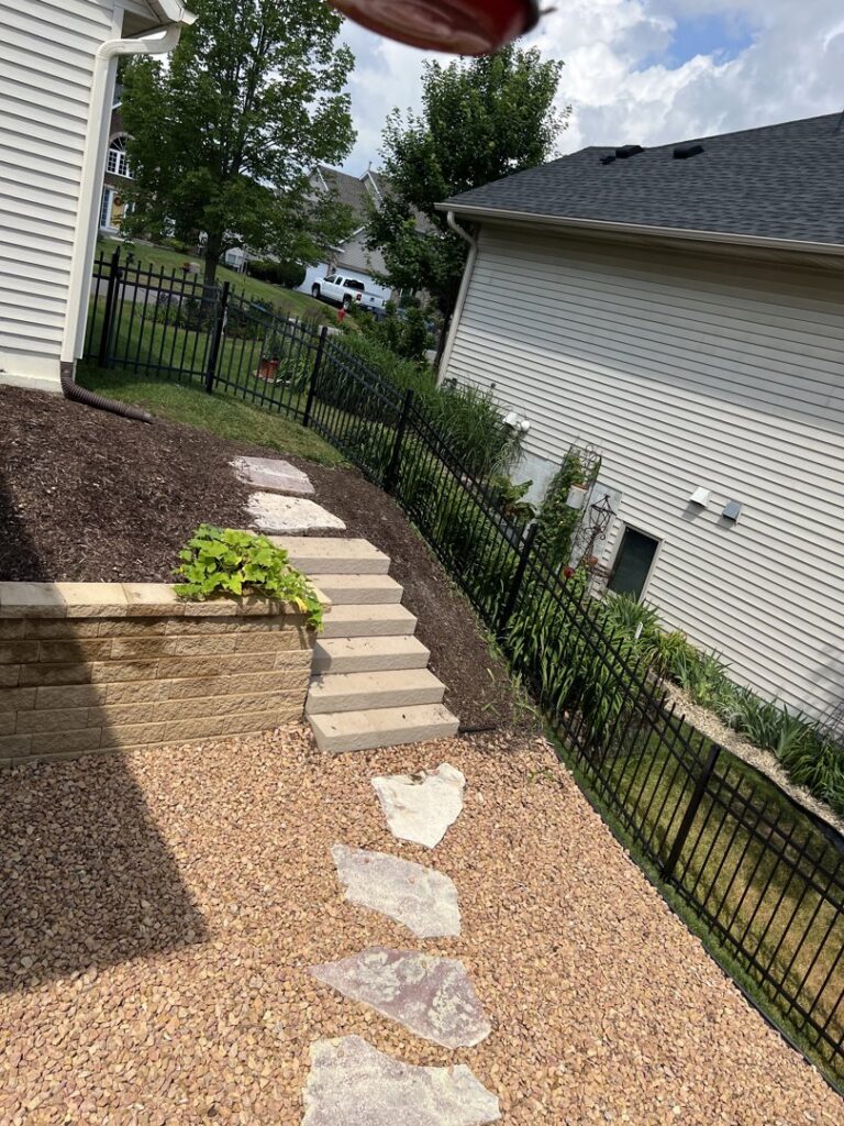 A black metal fence running along a sloped backyard with a retaining wall, installed by Mauer Company in Little Canada, MN.