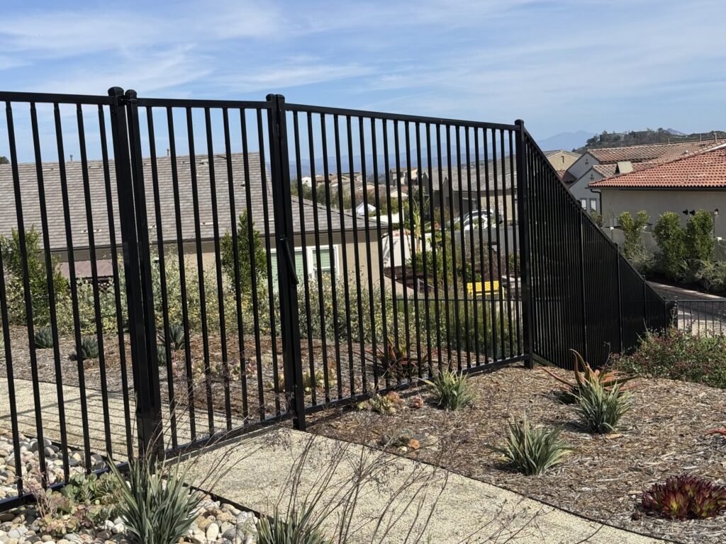 A black metal fence installed on a sloped landscape by Gates Access Solutions in San Diego, CA
