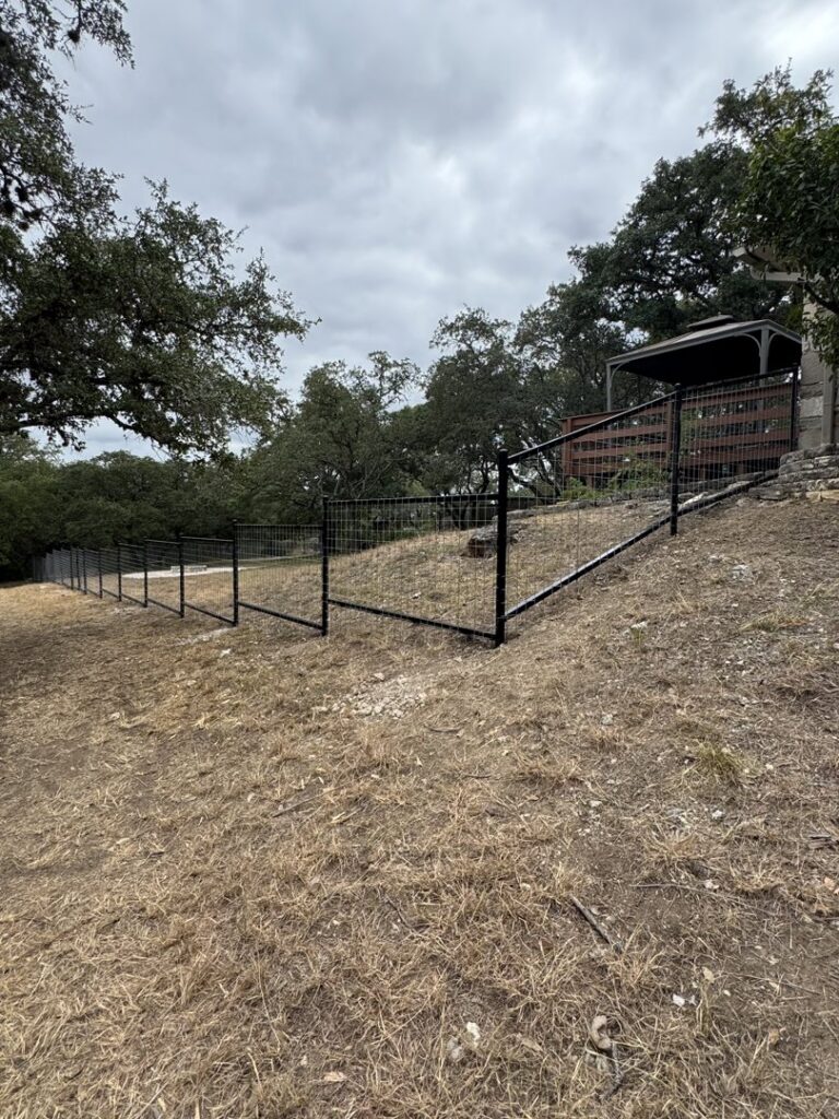 A black metal fence installed on sloped terrain by Liberty Fence & Stain in San Antonio, TX.