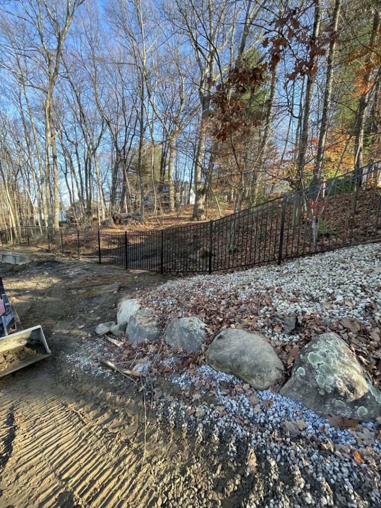 A newly installed black metal fence on a sloped, wooded terrain by Vision One Construction in Schenectady, NY