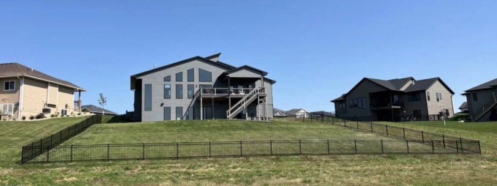 A black ornamental metal fence installed on a sloped residential property by The GateKeeper Perimeter Fence & Automated Security in Sioux Falls, SD