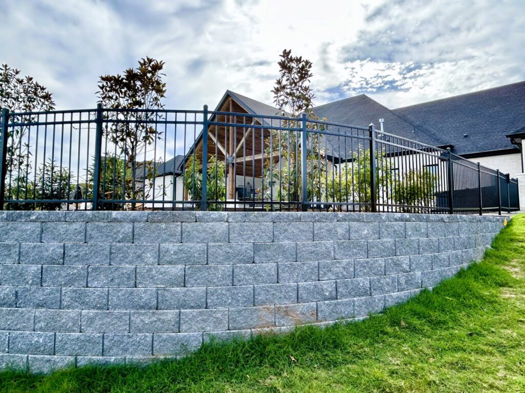 A black metal fence expertly installed on top of a stone retaining wall by The Fence Man in Fort Smith, AR.