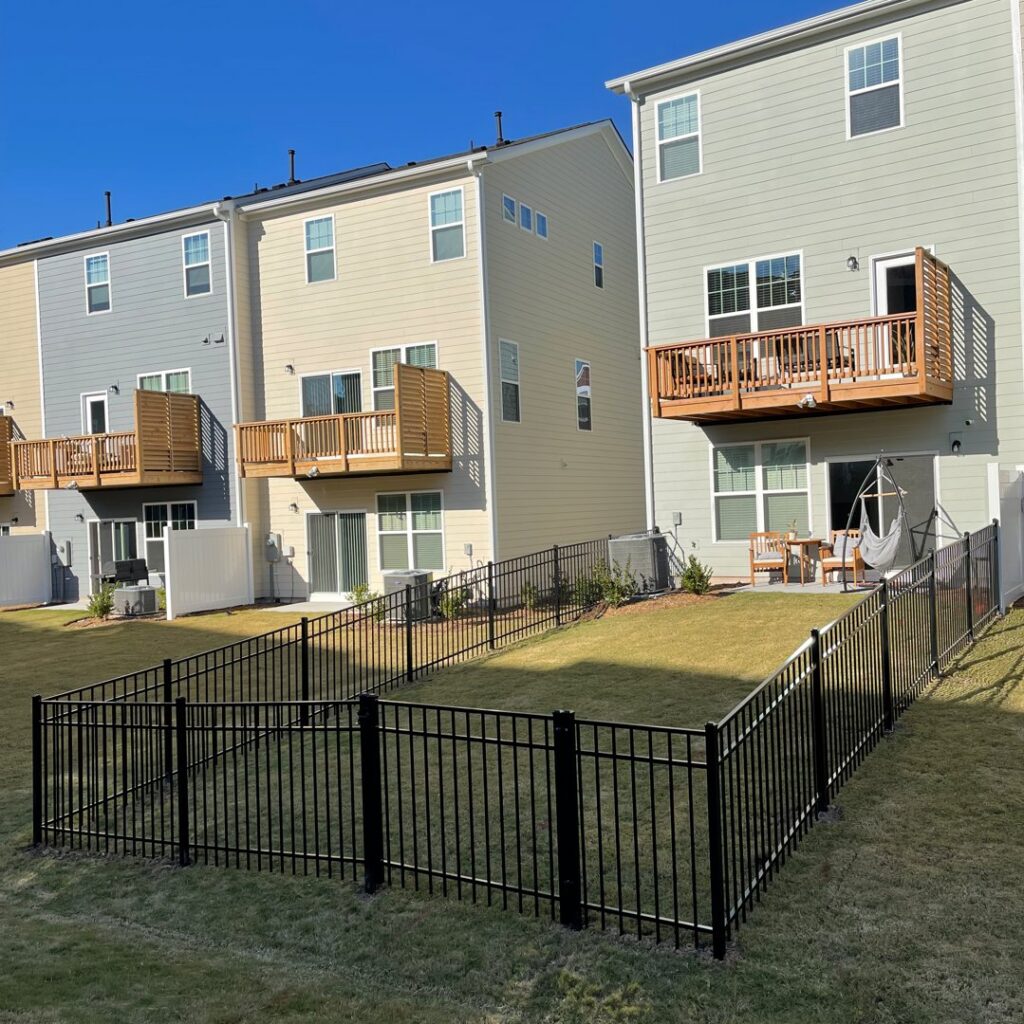 A black metal fence enclosing a small backyard area behind townhouses, installed by Align Fence Builders in Durham, NC.