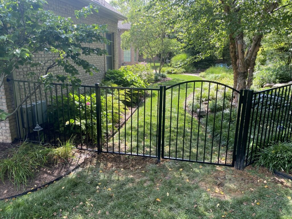 A black ornamental metal fence with an arched gate installed next to a brick house by Nailed It Fencing and Exteriors in Evansville, IN.