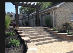 A black metal fence with a gate integrated with a stone staircase and pergola by Snyders Custom Fencing in York, PA.