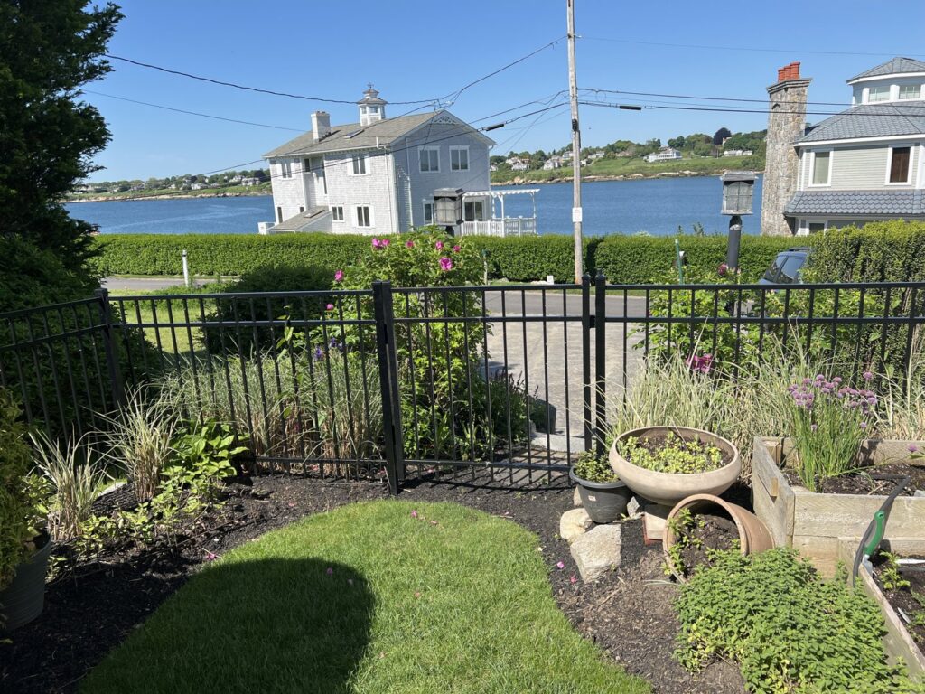 A black metal fence with a gate overlooking a waterfront property, installed by Fence Company of Rhode Island in Providence, RI.