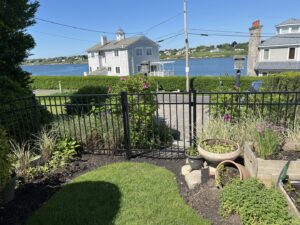 A black metal fence with a gate overlooking a waterfront property, installed by Fence Company of Rhode Island in Providence, RI.