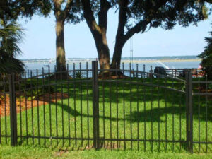 A beautiful black metal fence with an arched gate overlooking a waterfront view, installed by Palmetto Fence Co in North Charleston, SC.