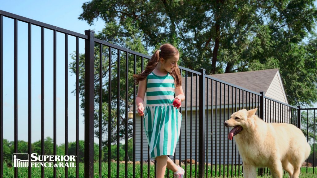 A young girl and a white dog playing next to a newly installed black metal fence by Superior Fence and Rail of Little Rock, AR