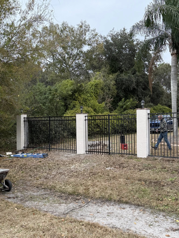 A newly installed black metal fence with decorative pillars and a gate by Native Outdoors, LLC in Orlando, FL.